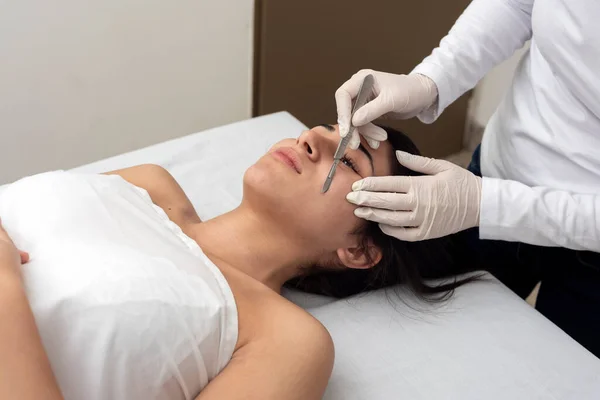 young woman lying on a stretcher in an aesthetic center performing facial and body beauty and aesthetic treatment with dermapen and dermaplaning techniques with scalpel