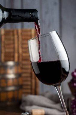 Bir kadeh kırmızı şarap ve bir şişe şarap. Üzüm fıçısı mantarı ve ahşap tahtalarda servis edilen şarap bardağı..