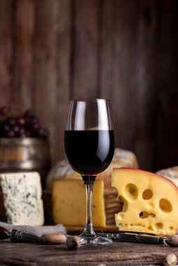 Bir kadeh kırmızı şarap ve bir şişe şarap. Üzüm fıçısı mantarı ve ahşap tahtalarda servis edilen şarap bardağı..