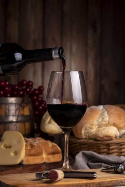 Bir kadeh kırmızı şarap ve bir şişe şarap. Üzüm fıçısı mantarı ve ahşap tahtalarda servis edilen şarap bardağı..