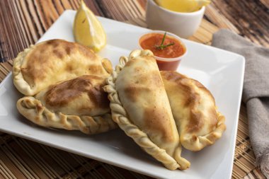 Ev yapımı börekler tavuk eti sebze, jambon ve peynirli ahşap tabakta sos ve limonla pişiriliyor. 