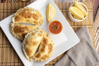 Ev yapımı börekler tavuk eti sebze, jambon ve peynirli ahşap tabakta sos ve limonla pişiriliyor. 