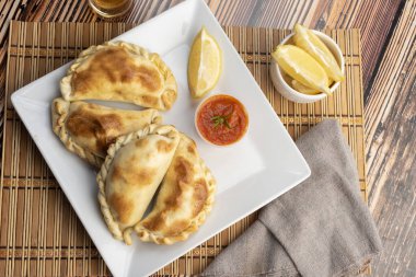 Ev yapımı börekler tavuk eti sebze, jambon ve peynirli ahşap tabakta sos ve limonla pişiriliyor. 