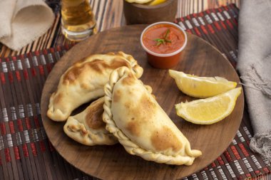 Ev yapımı börekler tavuk eti sebze, jambon ve peynirli ahşap tabakta sos ve limonla pişiriliyor. 