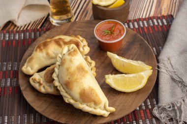 Ev yapımı börekler tavuk eti sebze, jambon ve peynirli ahşap tabakta sos ve limonla pişiriliyor. 