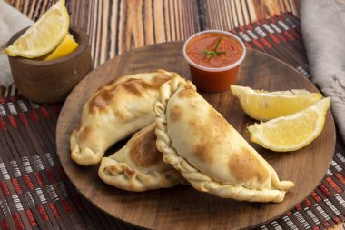 Ev yapımı börekler tavuk eti sebze, jambon ve peynirli ahşap tabakta sos ve limonla pişiriliyor. 