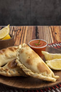 Ev yapımı börekler tavuk eti sebze, jambon ve peynirli ahşap tabakta sos ve limonla pişiriliyor. 
