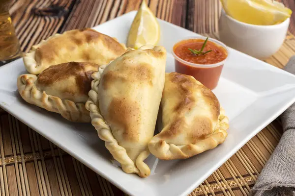 Ev yapımı börekler tavuk eti sebze, jambon ve peynirli ahşap tabakta sos ve limonla pişiriliyor. 