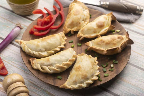 Homemade empanadas cooked with chicken meat vegetables and ham and cheese on a wooden plate with sauces and lemon