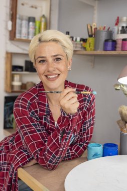 Genç kadın ressam çalışma alanını boyayan ve çizen boyalı elleriyle yaşam tarzından memnun. 