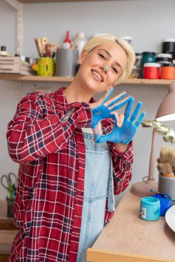 Genç kadın ressam çalışma alanını boyayan ve çizen boyalı elleriyle yaşam tarzından memnun. 