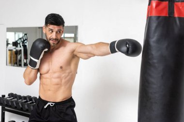 Spor salonundaki kaslı adam boks antrenmanı yapıyor. Çanta ve boks eldivenleriyle. 