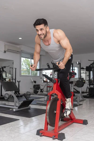 adult man in gym training with stationary bike barbell dumbbells for health and fitness