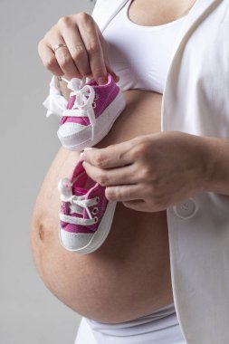 Karnında ve babasının göbeğinde bir çift küçük spor ayakkabısıyla karnını gösteren hamile bir kadın. 