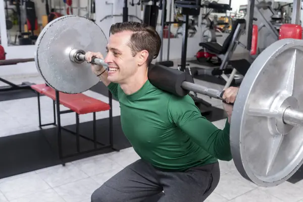 Spor salonunda halterli yetişkin bir adam sağlık ve zindelik eğitimi alıyor. 