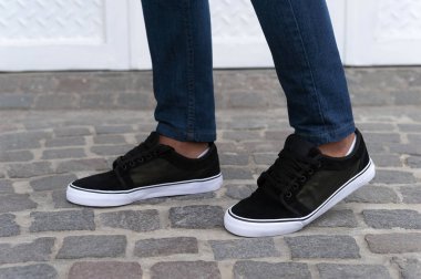 Adamın bacakları farklı renklerde ve kot pantolonlu şık spor ayakkabılar. 