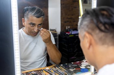 Adam aynanın önünde makyaj yapıyor. Resim ve makyaj atölyesinde. Ölüleri anmak için yüzünü boyuyor. 