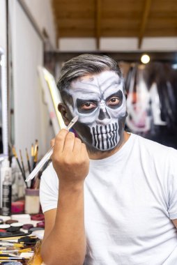 Adam aynanın önünde makyaj yapıyor. Resim ve makyaj atölyesinde. Ölüleri anmak için yüzünü boyuyor. 