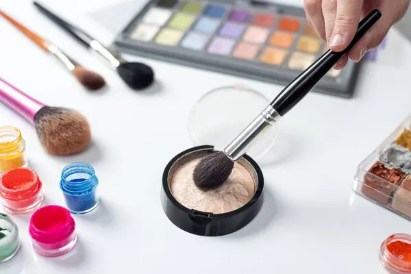 set of cosmetic makeup for lips, eyes, cheeks and face with makeup brushes with hand holding a brush