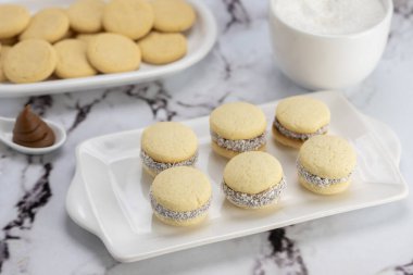 Koyu ve beyaz çikolatalı alfajore ve mısır nişastalı hindistancevizi rendelenmiş, kahvaltı masasında bir fincan süt ve kahve veya atıştırmalık 