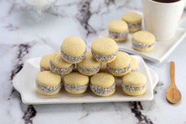 Koyu ve beyaz çikolatalı alfajore ve mısır nişastalı hindistancevizi rendelenmiş, kahvaltı masasında bir fincan süt ve kahve veya atıştırmalık 