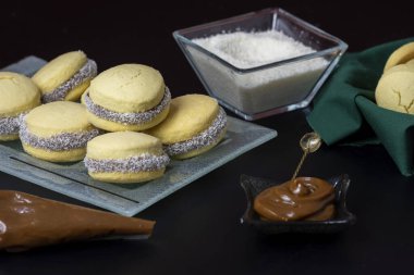 Koyu ve beyaz çikolatalı alfajore ve mısır nişastalı hindistancevizi rendelenmiş, kahvaltı masasında bir fincan süt ve kahve veya atıştırmalık 