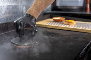 Adım adım hamburgerler üretiyor ve pişiriyor. Taze ev yapımı kıyma tezgahının sonuna kadar. Eldivenleri demir tabakta patates ve çedar peynirli patates kızartması ve patates kızartmasıyla pişirilmiş patates ekmeği olan bir şef tarafından yapıldı. 