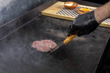 Adım adım hamburgerler üretiyor ve pişiriyor. Taze ev yapımı kıyma tezgahının sonuna kadar. Eldivenleri demir tabakta patates ve çedar peynirli patates kızartması ve patates kızartmasıyla pişirilmiş patates ekmeği olan bir şef tarafından yapıldı. 