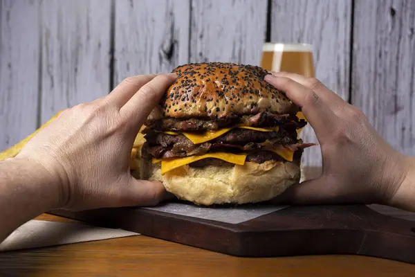 hands holding a large meat burger with cheese ham bacon onion tomato potato bun cheddar lettuce french fries