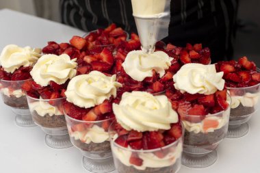 pastry woman assembling cakes and desserts step by step with fruits of the forest with cream decorating a cake and sweet glasses 