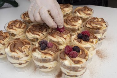pastry woman assembling cakes and desserts step by step with fruits of the forest with cream decorating a cake and sweet glasses 