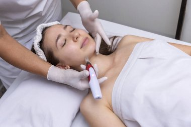 Estetik bir merkezde sedyede yatan genç bir kadın cilt bakımı ve cilt bakımı teknikleriyle estetik ve estetik tedavi görüyor. 