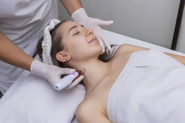 young woman lying on a stretcher in an aesthetic center undergoing facial beauty and aesthetic treatment with dermapen and dermaplaning techniques