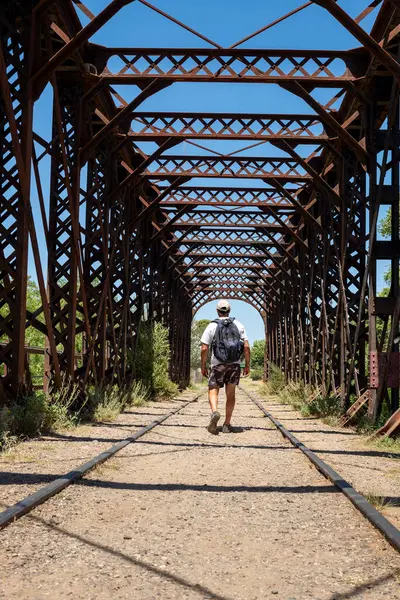 man walking on an old iron bridge over the train tracks