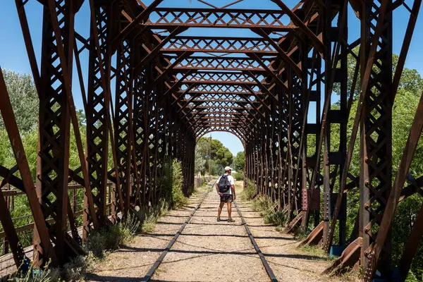 man walking on an old iron bridge over the train tracks