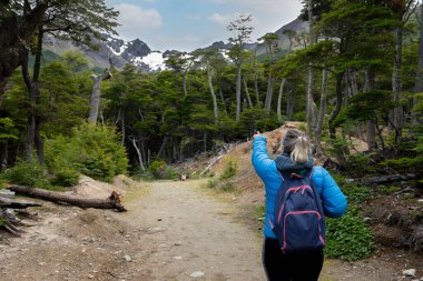 Kadın, dağların güzel manzarasını seyrediyor ve yürüyor. Ormanlar, nehirler ve köprüler. Uhuaia Argentina 'nın dünyanın sonu.