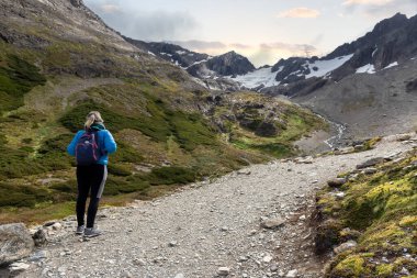 Kadın, dağların güzel manzarasını seyrediyor ve yürüyor. Ormanlar, nehirler ve köprüler. Uhuaia Argentina 'nın dünyanın sonu.