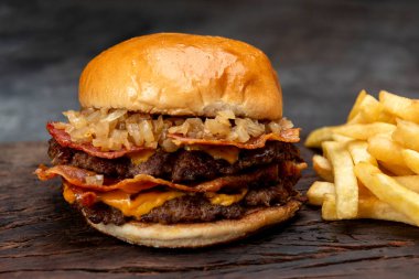 Salatalık soslu ev yapımı sığır burger domates peyniri, marul, ketçap, hardal, patates ekmeği ve tahta üzerinde patates kızartması. 