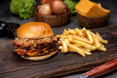 Salatalık soslu ev yapımı sığır burger domates peyniri, marul, ketçap, hardal, patates ekmeği ve tahta üzerinde patates kızartması. 