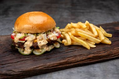 Salatalık soslu ev yapımı sığır burger domates peyniri, marul, ketçap, hardal, patates ekmeği ve tahta üzerinde patates kızartması. 