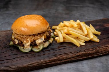 Salatalık soslu ev yapımı sığır burger domates peyniri, marul, ketçap, hardal, patates ekmeği ve tahta üzerinde patates kızartması. 