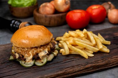 Salatalık soslu ev yapımı sığır burger domates peyniri, marul, ketçap, hardal, patates ekmeği ve tahta üzerinde patates kızartması. 