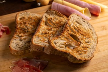 Sağlıklı, organik, bütün ve dilimlenmiş ev yapımı ekmek, ahşap bir masa üzerinde jambon ve peynir ve kabuklu mutfak gereçleri.. 