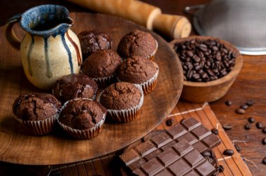 Sıvı çikolatalı kekler ve kakao tozlu dulce de leche, çikolatalı gofret ve mutfak gereçleri olan ahşap bir masada kahve çekirdekleri.. 