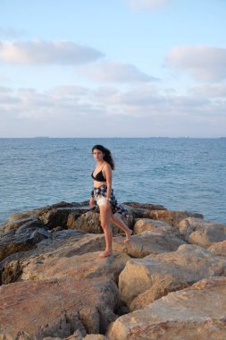 Siyah mayolu kız kayalık bir sahilde poz veriyor.