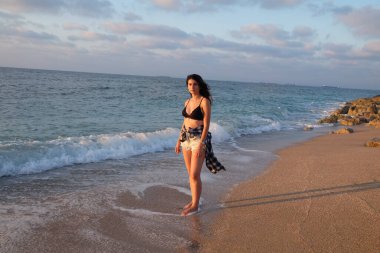 Güneşli bir günde kumsalda yürüyen siyah bikinili bir kadın.