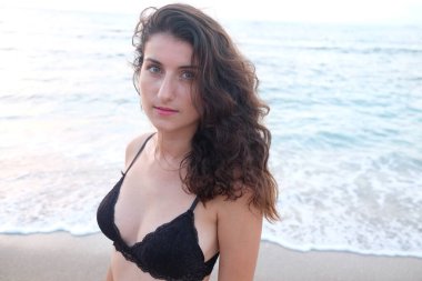 Plajda siyah atkısı olan siyah bikinili güzel bir kız.