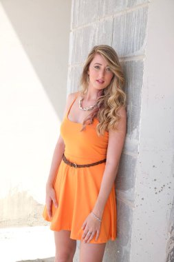 Şehirde sokakta poz veren turuncu elbiseli güzel sarışın manken.