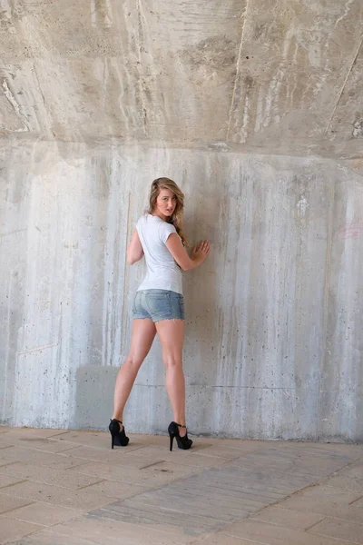 Endüstriyel arka planda poz veren beyaz elbiseli güzel sarışın.