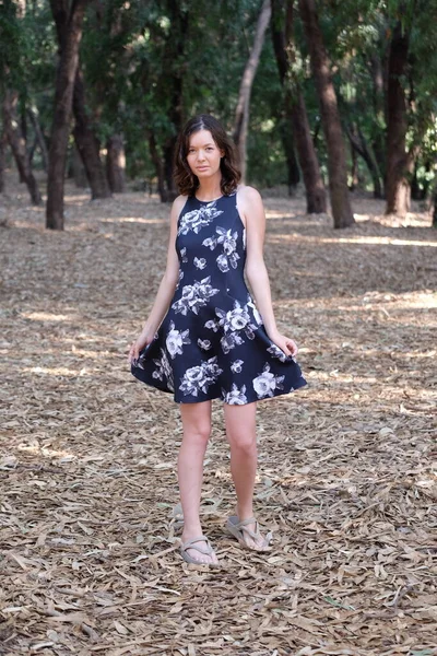 young woman with dark hair in black dress walking in the park